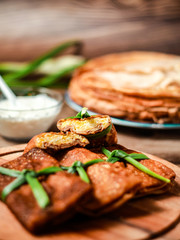 Two Parts Of Sliced Tasty stuffed russian thin crepes with tuna, potatoes, cheese, eggs and green onion decoration On The Wooden Cutting Board. Vertical Orientation.