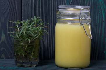 Lemon Kurd in a glass jar. Nearby a bunch of rosemary in a glass. Against the background of brushed boards.