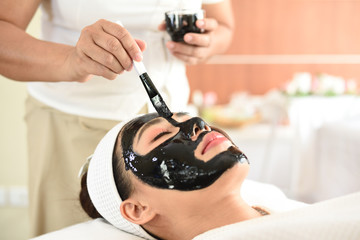 Obraz na płótnie Canvas wellness, beauty and relaxation concept - young woman face mask with black mud on table at spa