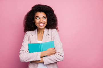 Photo of funny pretty dark skin lady hold journal book close to chest look side empty space imagination flight wear checkered blazer isolated pastel pink color background