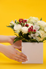 cropped view of woman holding spring fresh bouquet of flowers in box on yellow background