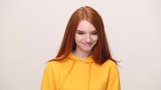 Pretty ginger curly young girl in yellow streetwear hoodie posing isolated on white background in studio. People sincere emotions lifestyle concept. Looking at camera approvingly at camera nod head