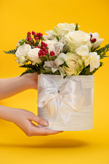 Fototapeta na wymiar cropped view of woman holding spring fresh bouquet of flowers in festive gift box with bow on yellow