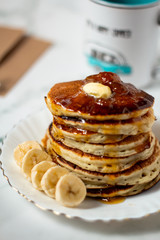Tasty breakfast with hot american pancakes with bananas, butter and apricot jam on the white table. Mug and envelope background