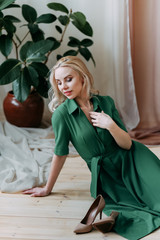 A beautiful happy cheerful attractive fragile sensitive tender blonde girl in a bright green spring dress poses twirls and smiles at the camera against a background of greenery and flowers