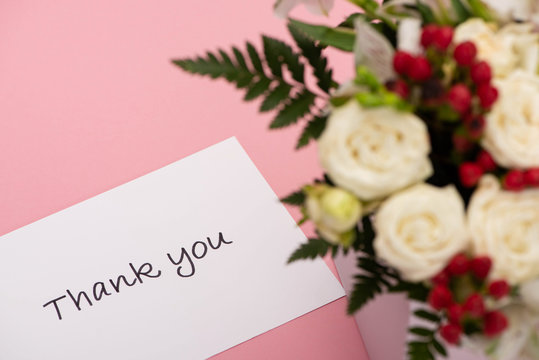 selective focus of bouquet of flowers in festive gift box near thank you greeting card on pink background