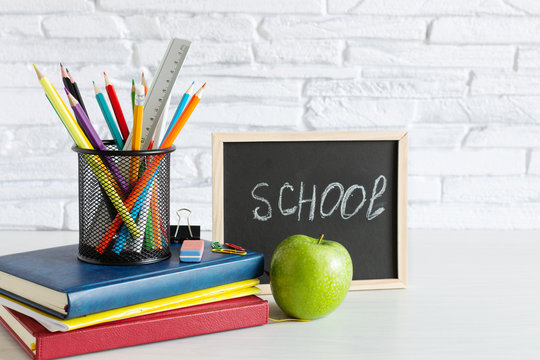 Back to school concept with books, colorful pencils and apple on white wooden table.