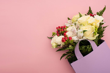 top view of bouquet of flowers in violet paper bag on pink background