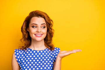 Closeup photo of pretty wavy ginger lady holding open arm showing presenting novelty low price product wear retro style polka-dot blue white shirt isolated yellow color background