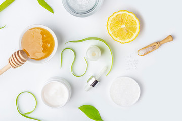 Natural organic ingredients to make home skin care. Cleansing and nourishing cosmetics. Beauty products: cream, honey, sea salt among green leaves on white background. Flat lay, copy space for text