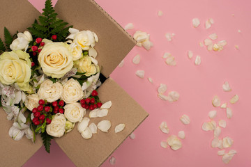 Fototapeta na wymiar top view of bouquet of flowers in cardboard box near scattered petals on pink background