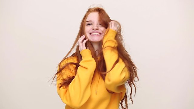 Happy charming ginger redhead curly young girl in yellow streetwear hoodie posing isolated on white background in studio. People emotions lifestyle concept. Looking at camera smiling shaking her head