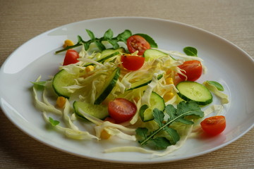 Fresh and healthy vegetable salad with cabbage, tomatoes, cucumbers, corn and arugula.