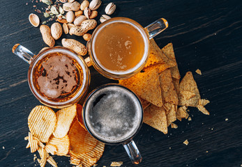 three glasses of expensive craft beer, classic and unfiltered and dark in a glass on the table with a snack of peanut and pistachio chips and nachos