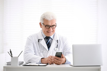 Senior doctor with smartphone at table in office