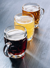 three glasses of expensive craft beer, classic and unfiltered and dark in a glass on the table with a snack of peanut and pistachio chips and nachos