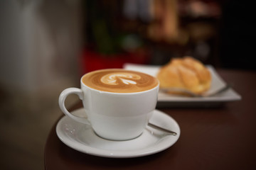 white cup with cappuccino on a brown table