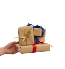 hand holds a stack of wrapped gifts in brown craft paper with tied silk bows