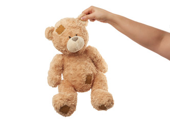 female hand holds the ear of a big beige cute teddy bear with patches