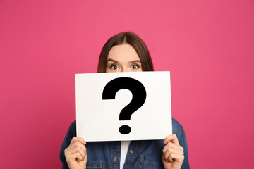 Emotional woman holding question mark sign on pink background - obrazy, fototapety, plakaty