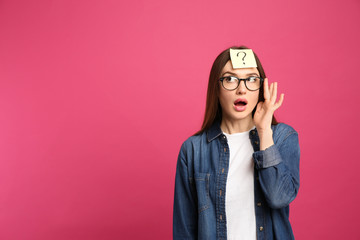 Emotional woman with question mark sticker on forehead against pink background. Space for text