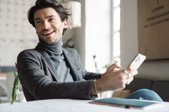Image of handsome caucasian young man smiling and using cellphone in cafe