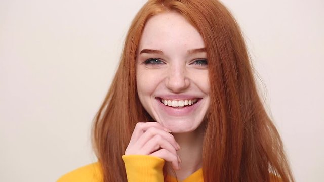 Close up happy charming ginger redhead curly young girl in yellow streetwear hoodie posing isolated on white background in studio. People sincere emotions lifestyle concept. Looking at camera smiling