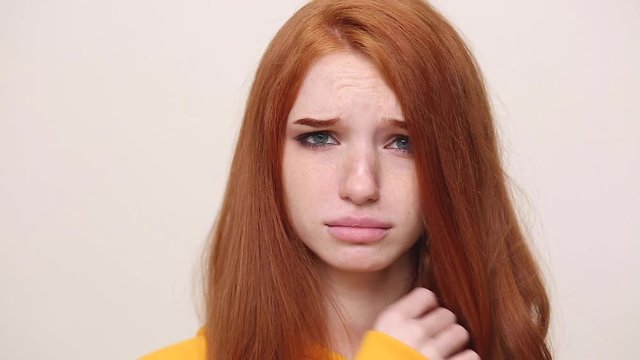Close up confused sad upset crying ginger redhead curly young girl in yellow streetwear hoodie posing isolated on white background in studio. People sincere emotions lifestyle concept. Look at camera