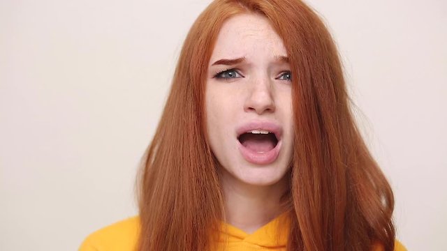 Close up fun sad upset crying ginger redhead curly young girl in streetwear hoodie posing isolated on white background in studio. People sincere emotions lifestyle concept. Look at camera screaming