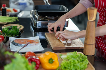 Hand of woman and pepper bottles made of wood cooking delicious salmon steak at the kitchen.