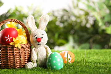 Colorful Easter eggs, toy rabbit and daffodil flowers in green grass. Space for text