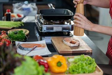 Hand of woman and pepper bottles made of wood cooking delicious salmon steak at the kitchen.