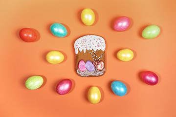 Festive Easter composition of bright multicolored eggs and gingerbread Easter cake on orange background. Painted eggs and Easter cake are Easter symbols. Top view, flat lay.