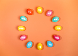 Bright multicolored glossy Easter eggs laid out in circle on trendy orange background. Creative festive Easter background. Painted eggs as symbols of Easter. Top view, flat lay, copy space.