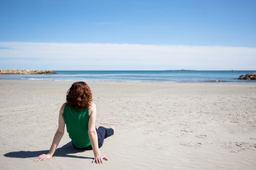 Woman sitting on the sand on the beach looking at the sea