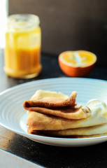 Thin Pancakes on the white plate with Orange Curd Jar on dark background and a half of orange vertical orientation