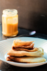Thin Pancakes on the white plate with Orange Curd Jar on dark background vertical orientation