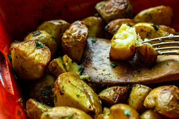 Fork cutting a baked potato wedge on the wooden spatula. Baked with spices, chopped garlic, olive oil and fresh chopped dill and green onion in a baking dish. Side view. Horizontal orientation