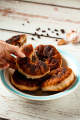 Hand holding a piece of belyash. Tasty homemade fried dough with minced meat. Pies are on a white and blue plate on a wooden table. Black peppercorns and garlic background. Copy space. 