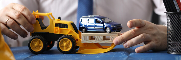Fototapeta na wymiar Close-up of male hands modifying and showing restructuring of parking in city. Architect handling toy yellow excavator. Transportation service. Business and building concept