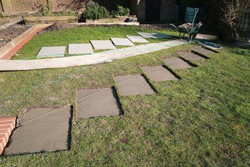 Rectangular sections cut into a lawn with concrete bases prepared for stepping stones. A string...
