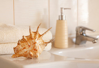 Сockleshell and Bath white cotton towels, ceramic bottle on Blurred bathroom interior background with sink and faucet.