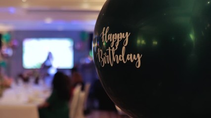 Happy Birthday helium balloon at banquet with singer in blurry background