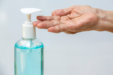Senior woman's hand is using bottle of sanitizer gel pump dispenser to wash her hands in grey background. Close up & Macro shot, Select focus, Prevention from covid19, Bacteria, healthcare concept
