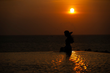 Fototapeta na wymiar Silhouette of woman relax in swimming pool by the sea Sunset time, Lifestyle concept Of a happy life.
