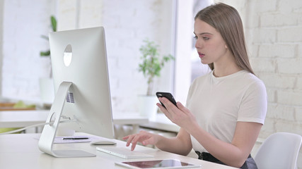 Young Woman using Smartphone and working on Desktop