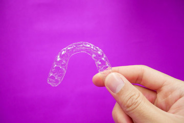 hand holding clear plastic retainer teeth that isolated on purple  background. it's an equipment for orthodontist give the patient to orthodontic surgery in dental clinic or hospital