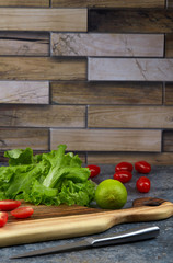 Cherry tomatoes cut in half lie on an elegant chopping Board on a dark kitchen table against a background of lettuce leaves. Preparation of summer dishes and salads. Vertical. Copy space.