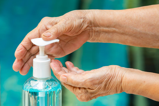 Senior woman's hands is pressing bottle of sanitizer gel pump dispenser to wash her hands in blue pool background, Close up & Macro shot, Select focus, Prevention from covid19, Bacteria, Healthcare