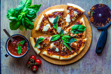 Pizza Margherita on a wooden table with pizza sauce, green basil, cherry tomatoes top view